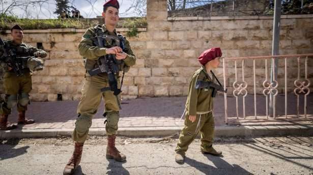 Joodse kolonistenjongen in Poerim-kostuum als IDF-parachutist naast een origineel - in Hebron.